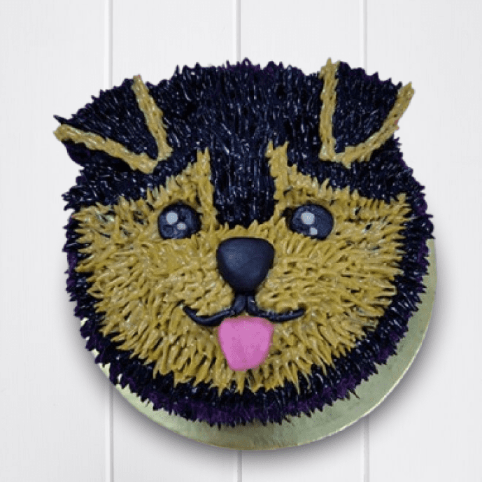Round dog birthday cake designed like a cute puppy face with black and tan fur, pink tongue, and shiny eyes