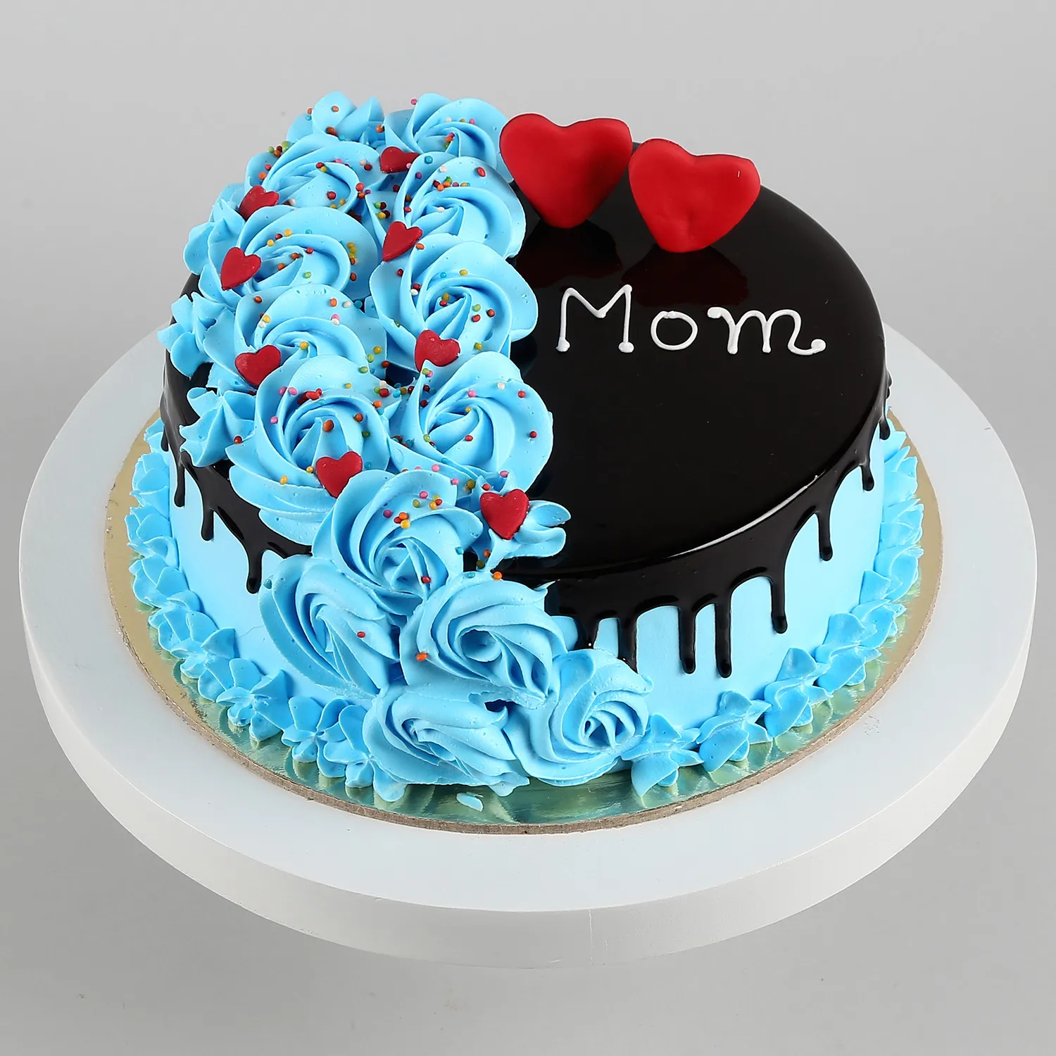Mother’s Day cake with blue rosettes, chocolate glaze, red hearts, and “Mom” written on top