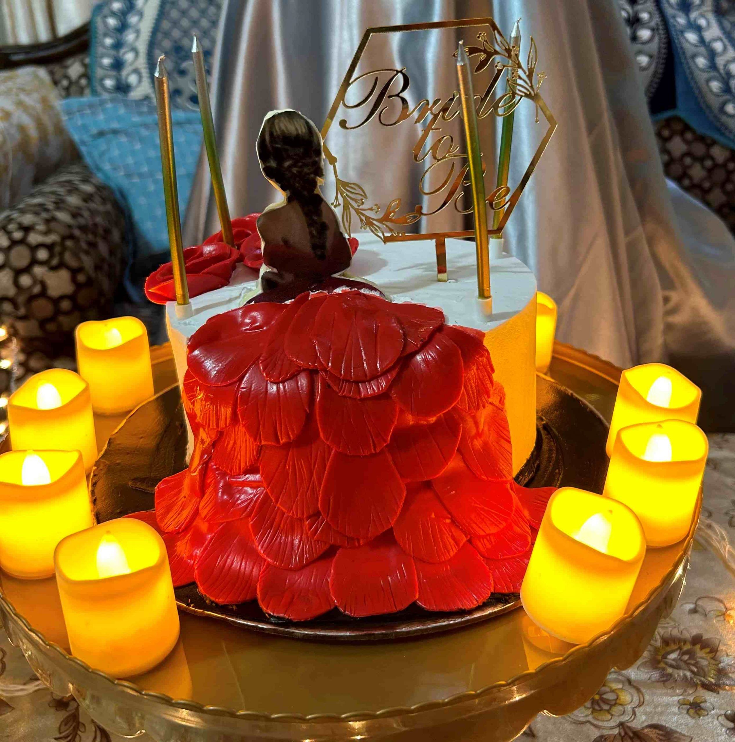 Bachelorette party cake with 'Bride to Be' topper and LED candles on a glass table.