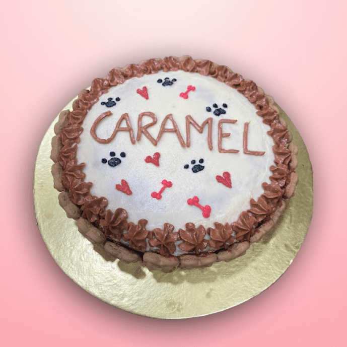 Caramel Paws dog birthday cake with heart, bone, and paw designs, frosted in white and brown with "CARAMEL" written on top.