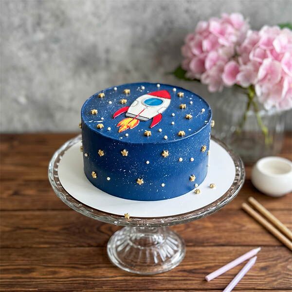 Dark blue galaxy cake with a red rocket illustration and tiny gold stars