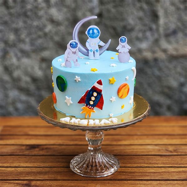 Sky blue space cake with astronaut toppers, a silver moon, and rocket art