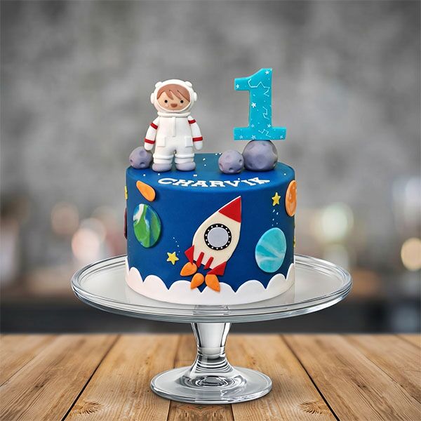 Blue space-themed cake with astronaut topper, rocket, and blue number one.