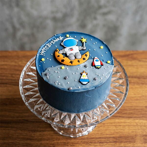Dark blue cream cake with astronaut on moon and rocket ship flat art.