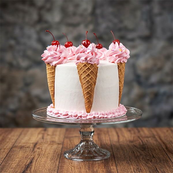 White cake decorated with pink frosting scoops in waffle cones topped with cherries.