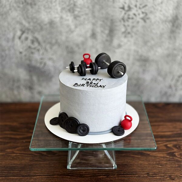 Grey frosted cake decorated with fondant dumbbells, weight plates, and kettlebells.