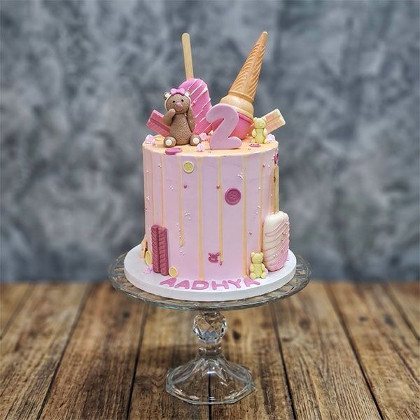 Pink 2nd birthday cake with a teddy bear, ice cream cone, and popsicle toppers.