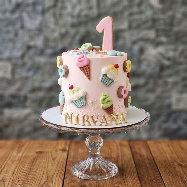 Pink 1st birthday cake with ice cream, cupcake, and donut toppers.