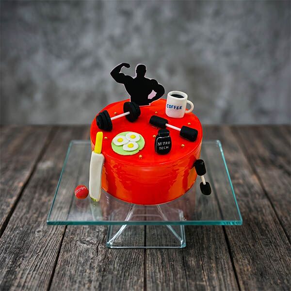 Glossy red fitness cake with fondant dumbbells, protein jar, and bodybuilder topper.