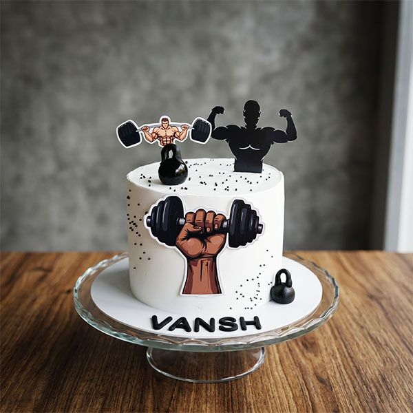 White cake with black sprinkles, kettlebells, barbell lifter graphic, and a custom name.