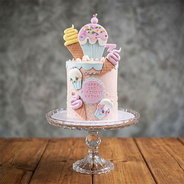 Tall pink 3rd birthday cake with fondant ice cream cones and cupcakes.