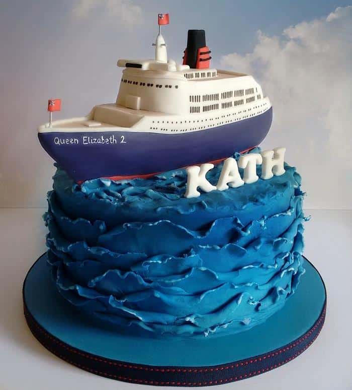 Ocean wave cruise ship cake with a Queen Elizabeth 2 ship model on top and name 'KATH' in fondant letters.